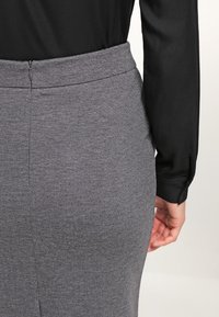 Grijze aansluitende rok met een soepele textuur en een ritssluiting aan de achterkant, gecombineerd met een zwart shirt met lange mouwen.