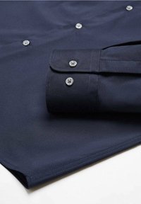 Chemise boutonnée bleu marine en tissu lisse avec un poignet plié, dotée de boutons ronds argentés et d'un ourlet droit.