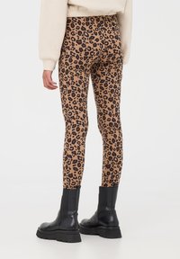 Leggings in stampa leopardata di colore sabbia con macchie nere, design a vita alta e tessuto elasticizzato, abbinati a stivali neri chunky.