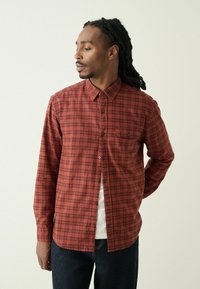 Punane ja must ruuduline pikkade varrukatega särk, millel on nööbiga krae ja rinnatasku. Kandtud valge T-särgi peal, koos tumedate teksadega.