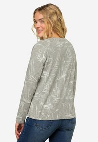 Jasnoszara bluzka z długim rękawem z nadrukiem żaglówki w białym kolorze. Posiada okrągły dekolt i luźny krój. Połączona z niebieskimi dżinsami.