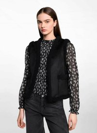 Svart väst med texturerad trim, med rundad halsringning, utan knäppningar och två framfickor, lager på lager över en mönstrad blus.