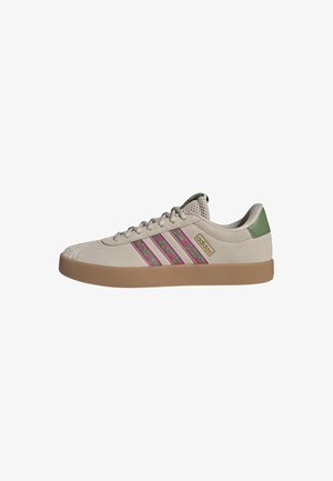 Zapatilla Adidas beige de caña baja con suela de goma, rayas camuflaje rosa y verde, lengüeta de malla y lengüeta trasera verde.