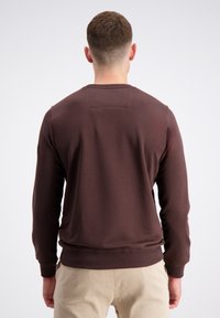 Bruine sweatshirt met een ronde hals, ribgebreide manchetten en zoom, met een eenvoudig ontwerp en zachte textuur, gedragen over beige broek.