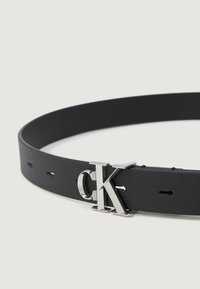Black leather belt featuring a silver CK logo buckle, smooth texture, and holes for adjustment, with a minimalist design.