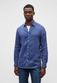 Ναυτικό μπλε πουκάμισο από λινό με κολάρο που κλείνει με κουμπιά, μακριά μανίκια και λευκά κουμπιά. Διαθέτει ελαφριά υφή και λεπτομέρεια με ετικέτα στο στρίφωμα.