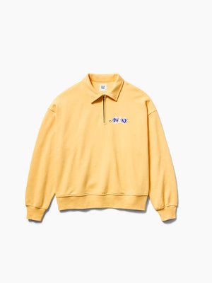 Κίτρινο φούτερ με μακριά μανίκια, φερμουάρ στο τέταρτο μέρος και γιακά, ριμπ μανσέτες και τελείωμα, με μπλε κείμενο «AWAKE» στο αριστερό μέρος του στήθους.