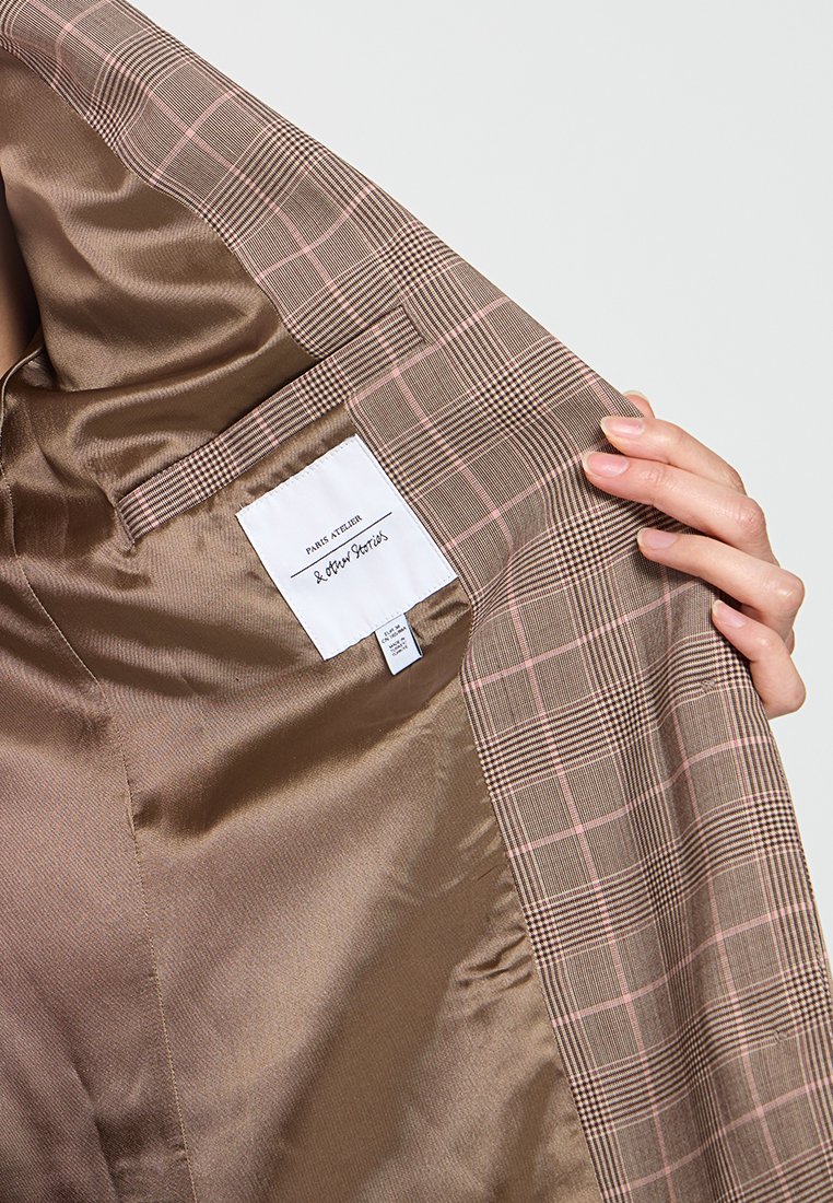Bruin geruite blazer met een satijnen afwerking aan de binnenkant. Heeft een gladde, glanzende textuur, een contrasterend geruit ontwerp met roze accenten en een label.