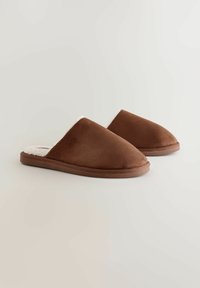 A barna tengeri bőrből készült mamuszok puha, fehér bolyhos béléssel rendelkeznek, slip-on kialakítással és lekerekített orral, valamint lapos, tartós talppal.