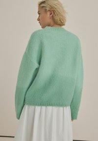 Mint green, oversized wool sweater with a soft, textured finish and ribbed cuffs, worn over a flowing white skirt.