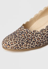 Scarpa piatta con stampa leopardata, bordi smerlati, schema di colori beige e nero, texture liscia e soletta imbottita con perforazioni.