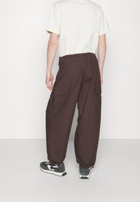 Bruine cargobroek met een relaxte pasvorm, elastische taille, zijzakken en boorden. Gecombineerd met een lichtkleurig t-shirt en grijze sneakers.