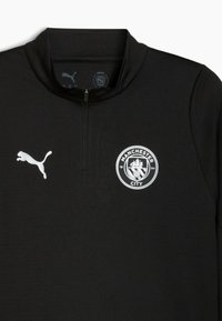 Sort sports pullover med halv lynlås, der har et hvidt Puma-logo og Manchester City-varemærke. Glat stof med en tætsiddende design.