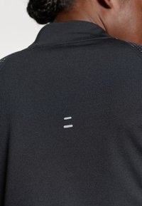 Must have mustreeritud must sportlik polo särk, millel on tekstuuritud kangas, krae ja minimalistlik hall logo seljal.