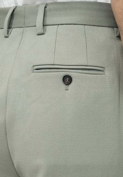 Κοντινή λήψη ανοιχτόγκρι παντελονιού με φινίρισμα, με πίσω τσέπη με πλαϊνή επένδυση και μαύρο κουμπί, καθώς και θηλιές για ζώνη στη μέση.