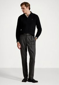 Μαύρο πουλόβερ πλεκτό με γιακά, σε συνδυασμό με γκρι μάλλινο παντελόνι. Μαύρα δερμάτινα παπούτσια ολοκληρώνουν την εμφάνιση, με κομψή, εφαρμοστή γραμμή.