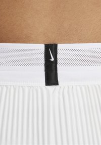 Bijele sportske kratke hlače imaju teksturirani pojas s crnom Nike etiketom. Tkanina izgleda lagano s horizontalnim nabranjima.