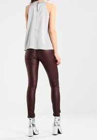 Grå ärmlös topp med hög krage, tillsammans med åtsittande bordeauxbyxor. Silverfärgade ankelskor har en blockklack och reflekterande yta.