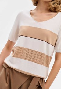 Korte mouwtrui van gebreid materiaal met een V-hals, met afwisselende strepen van beige en crème, en een gestructureerd beige gedeelte met perforaties.