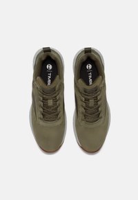 Zapatillas verde oliva con textura lisa, que cuentan con cordones, un cuello acolchado y una suela de goma con un acento contrastante. Logotipo en la plantilla.