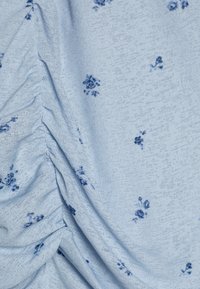 Lys blått stoff med en teksturert veving, med små mørkeblå blomster mønstre, samlet i seksjoner for å skape draperingsdetaljer.