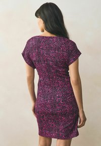 Kortärmad klänning i svart med ett rosa leopardmönster. Kroppsnära passform, knälång med sidslitsar. Slät, stretchig tygkvalitet.