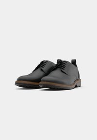 Pantofi din piele neagră cu o finisare netedă, design cu șireturi, vârf rotund și talpă din cauciuc maro. Stil minimalist cu un tab de prindere.