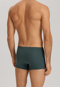 Calzoncillos de hombre en algodón verde oscuro con una textura suave, con un diseño ajustado y una cinturilla, mostrados desde la parte trasera.