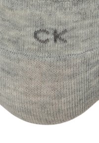 Siva pletena čarapa s mekanom teksturom, s blagim uzorkom i malim "CK" logom blizu vrha. Dizajn s okruglim prstom.