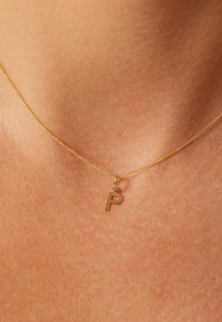 Collier en or avec une chaîne fine et un pendentif en forme de petite lettre majuscule "P". Texture lisse, design minimaliste.