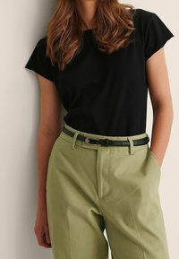 Černé tričko s krátkým rukávem v kombinaci s světle zelenými kalhotami s vysokým pasem a tmavozeleným koženým opaskem se stříbrnou sponou.