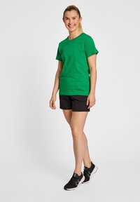 Grøn bomulds T-shirt med korte ærmer, parret med sorte shorts. Båret med sorte sportssko med hvide detaljer.
