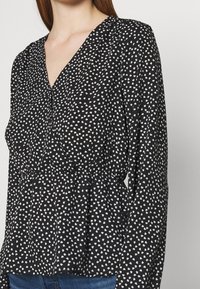 Haut noir à manches longues avec col en V, orné d'un motif de cœurs blancs et d'une taille cintrée, fabriqué en tissu léger.