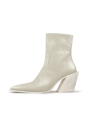 Botín beige de cuero con puntera puntiaguda y tacón alto grueso y angulado, mostrado de lado sobre un fondo blanco.