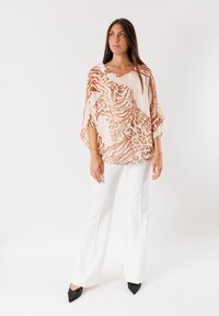 Top leggero e trasparente con un design fluido, caratterizzato da una base crema con stampe animali marroni. Abbinato a pantaloni bianchi e scarpe nere a punta.