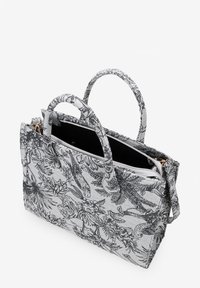 Bolsa de tela con estampado floral en blanco y negro, con dos asas, cierre con cremallera y superficie texturizada. El interior presenta un forro negro de contraste.