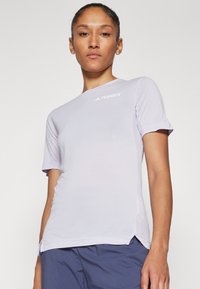 Camisola atlética de mangas curtas em lilás claro, com detalhes de malha nas laterais e gola redonda. Apresenta o logótipo "TERREX" em branco no peito.