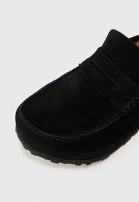 Sorte semsket slip-on sko med rund tå, dekorativ søm og gummisåle for godt grep. Minimalistisk design, ingen synlige logoer.