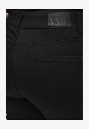 Jeans skinny negros con una textura suave. Presenta un parche con el logo de VMD en la cinturilla, detalle en el bolsillo trasero y un diseño ajustado.