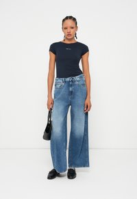 Ναυτική εφαρμοστή μπλούζα με κοντά μανίκια, σε συνδυασμό με υπερμεγέθεις ανοιχτό μπλε φαρδιές παντελόνες, με ελαφριά χρωματική κλιμάκωση και φθαρμένη υφή.