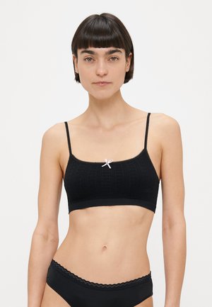 Bralette noir avec motif texturé, bretelles ajustables et bordure en dentelle. Présente un petit nœud blanc au centre devant.