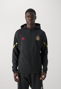 Schwarze Zip-Hoodie mit gefütterter Kapuze, gerippten Bündchen, gelben Akzenten und einem gestickten Atlanta United-Logo auf der Brust.