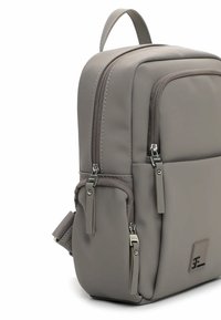 Szary plecak o gładkim, matowym wykończeniu, z dwoma zamykanymi na zamek kieszeniami, regulowanymi paskami i logo jako akcentem. Kompaktowy, prostokątny kształt.