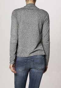 Grå långärmad topp med en strukturerad tyg och sjalkrage, i kombination med mörkblå tighta jeans som har bakfickor och sömdetaljer.