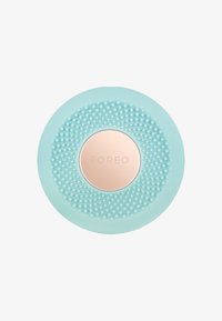 Sirkulær renseenhet i mintgrønn silikon, med en teksturert overflate av små prikker og en sentral logo plate i roségull.