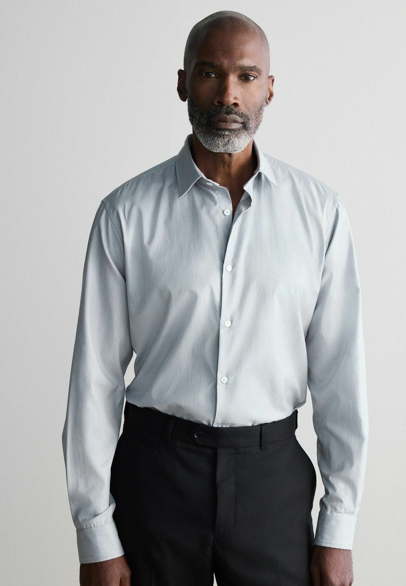Light gray button-up shirt with fine texture, long sleeves, and a classic collar. Paired with black dress pants.