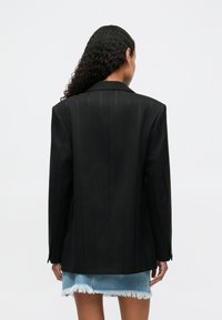 Mustvalge jope, millel on vertikaalsed triibud, kohandatud disain ja lõigatud krae, koos jeanise seelikuga, mille servad on hõrenenud.