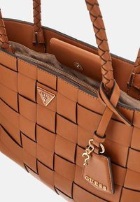 Borsa a tracolla intrecciata marrone con texture in pelle liscia, hardware dorato e dettaglio con charm. Presenta una chiusura con zip e manici intrecciati.