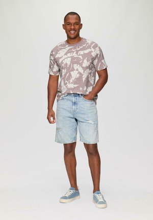 Camiseta de manga corta en un suave tono malva con un patrón de hojas blancas; pantalones cortos de denim azul claro con bordes deshilachados; zapatillas azules con suelas blancas.