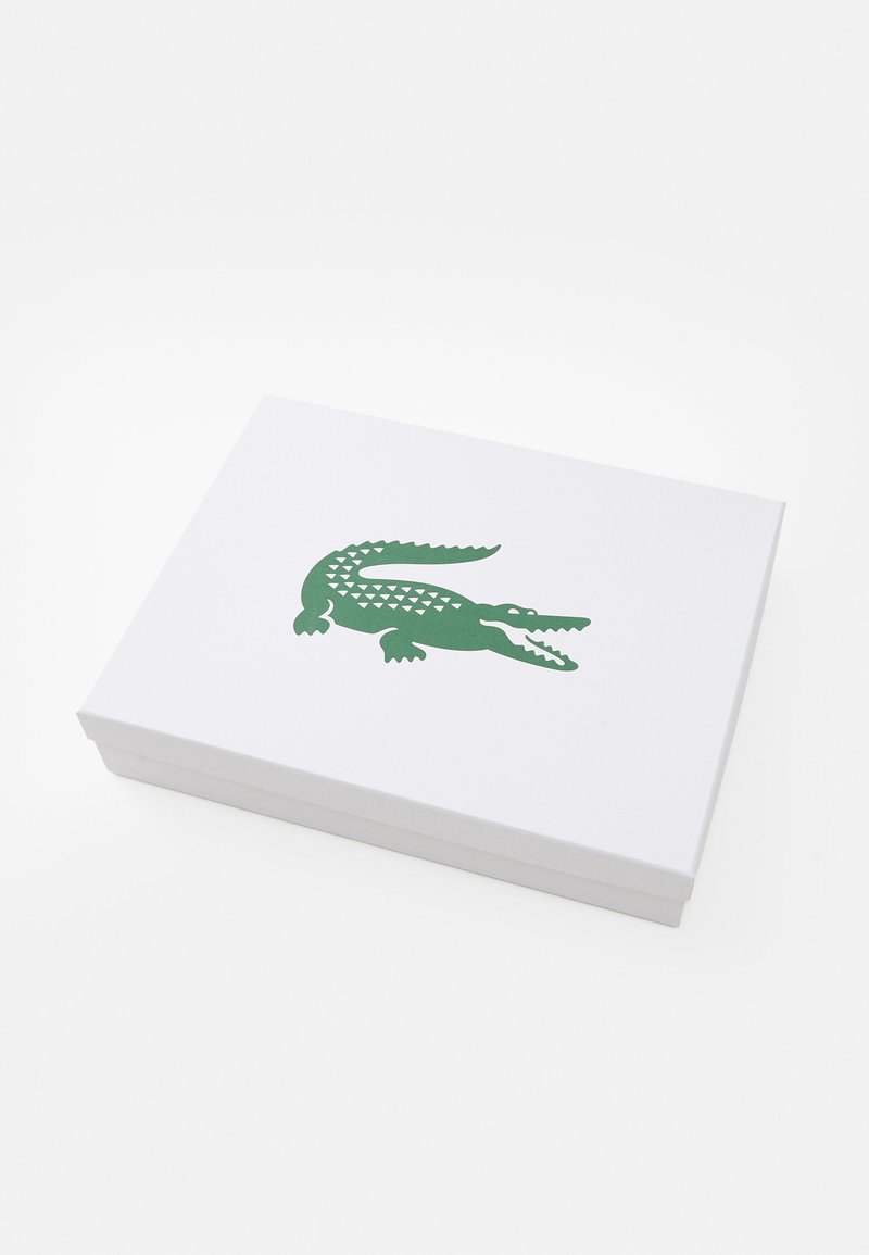 Weißer rechteckiger Karton mit einem grünen Krokodil-Logo, das auf den Deckel gedruckt ist, auf einer weißen Oberfläche platziert.